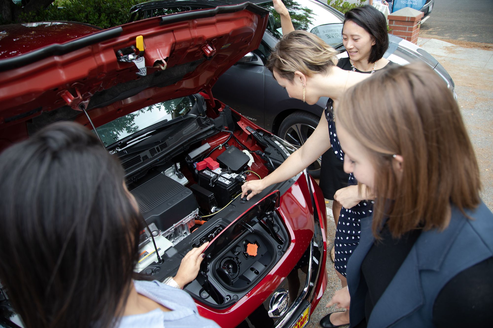 Four people looking under the hood of an electric vehicle