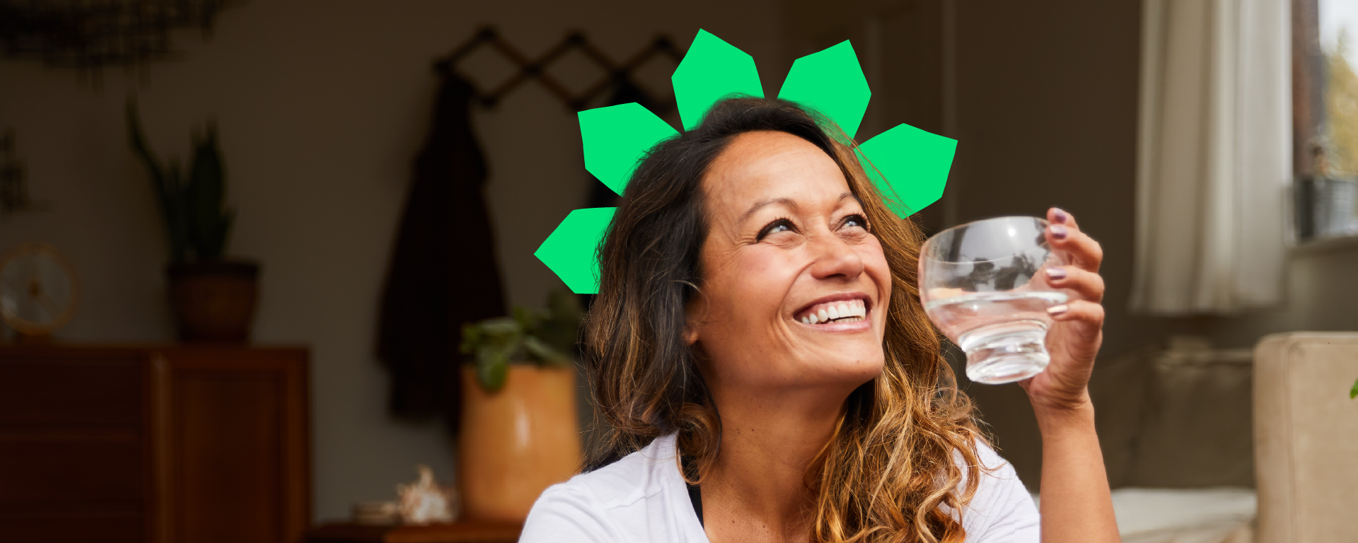A woman sits in the living room drinking a glass of water with an animated green crown on her head.
