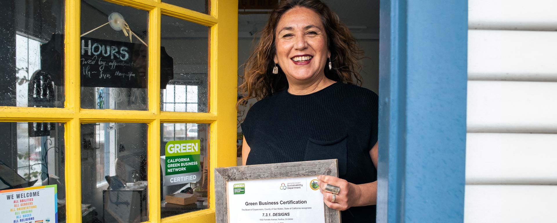 business owner holding Green Business Certification in doorway of her business in Pacifica