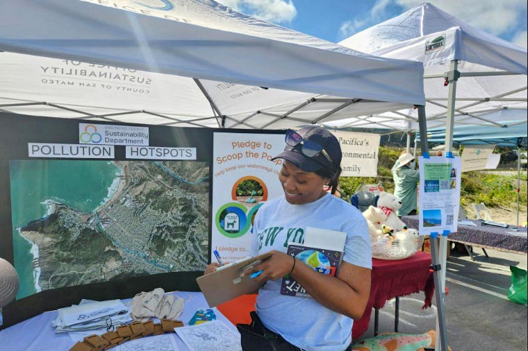 person signing Scoop the Poop pledge at San Mateo County Sustainability Department water protection booth at a community event